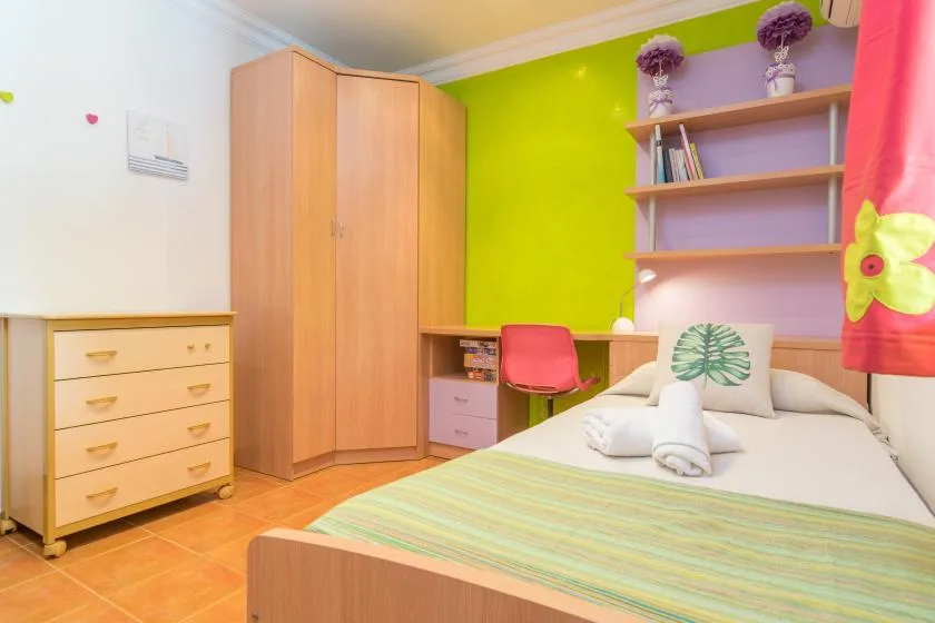 Un dormitorio colorido con una cama, un escritorio y estanterías.