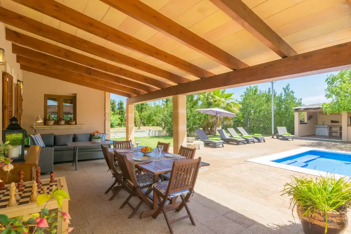 Una zona cubierta para comer y sentarse da a un patio soleado con piscina.