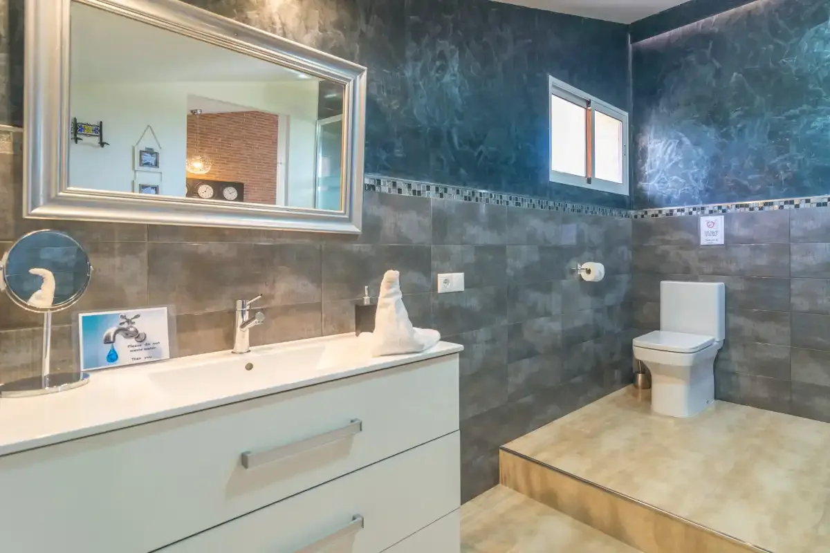 Un baño con lavabo, espejo grande e inodoro.