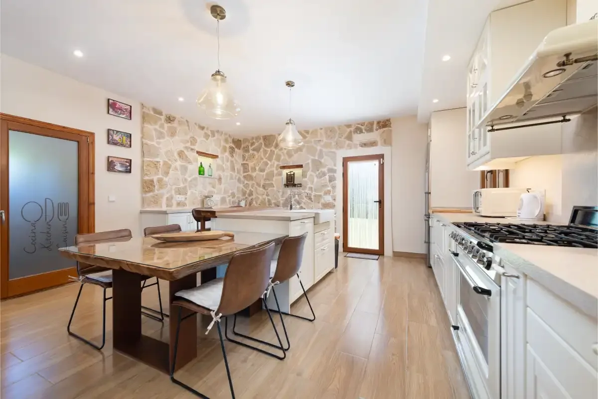 Una luminosa cocina con comedor tiene una mesa larga junto a una pared de piedra.