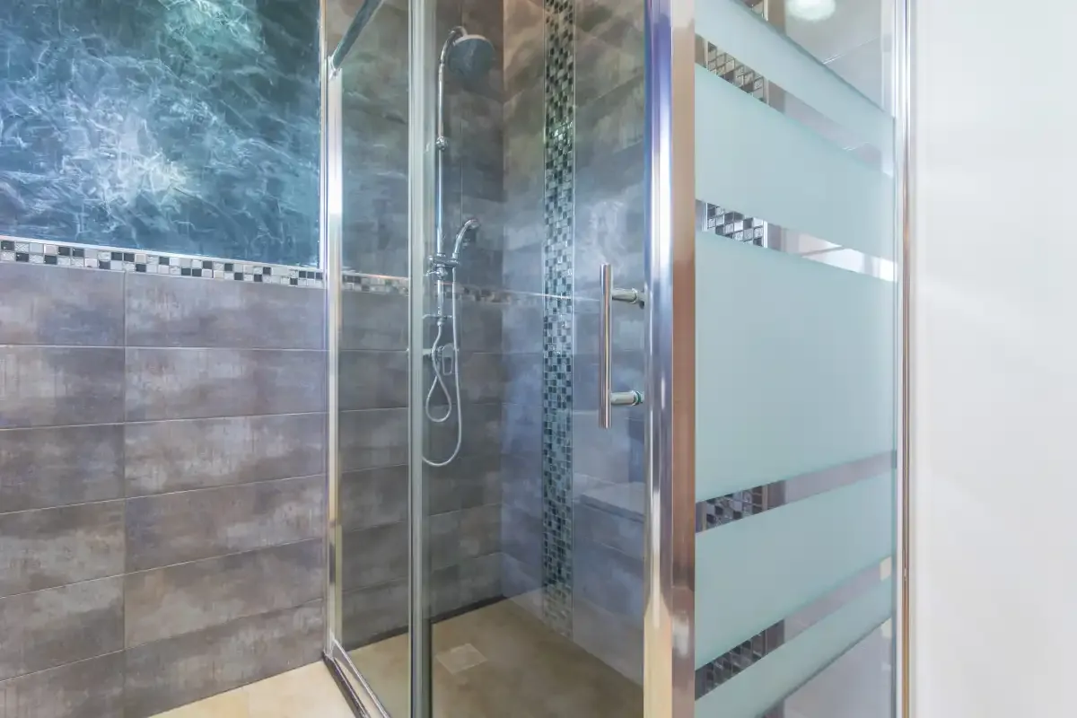 Una ducha de baño con azulejos, ducha de mano y paneles de vidrio esmerilado.