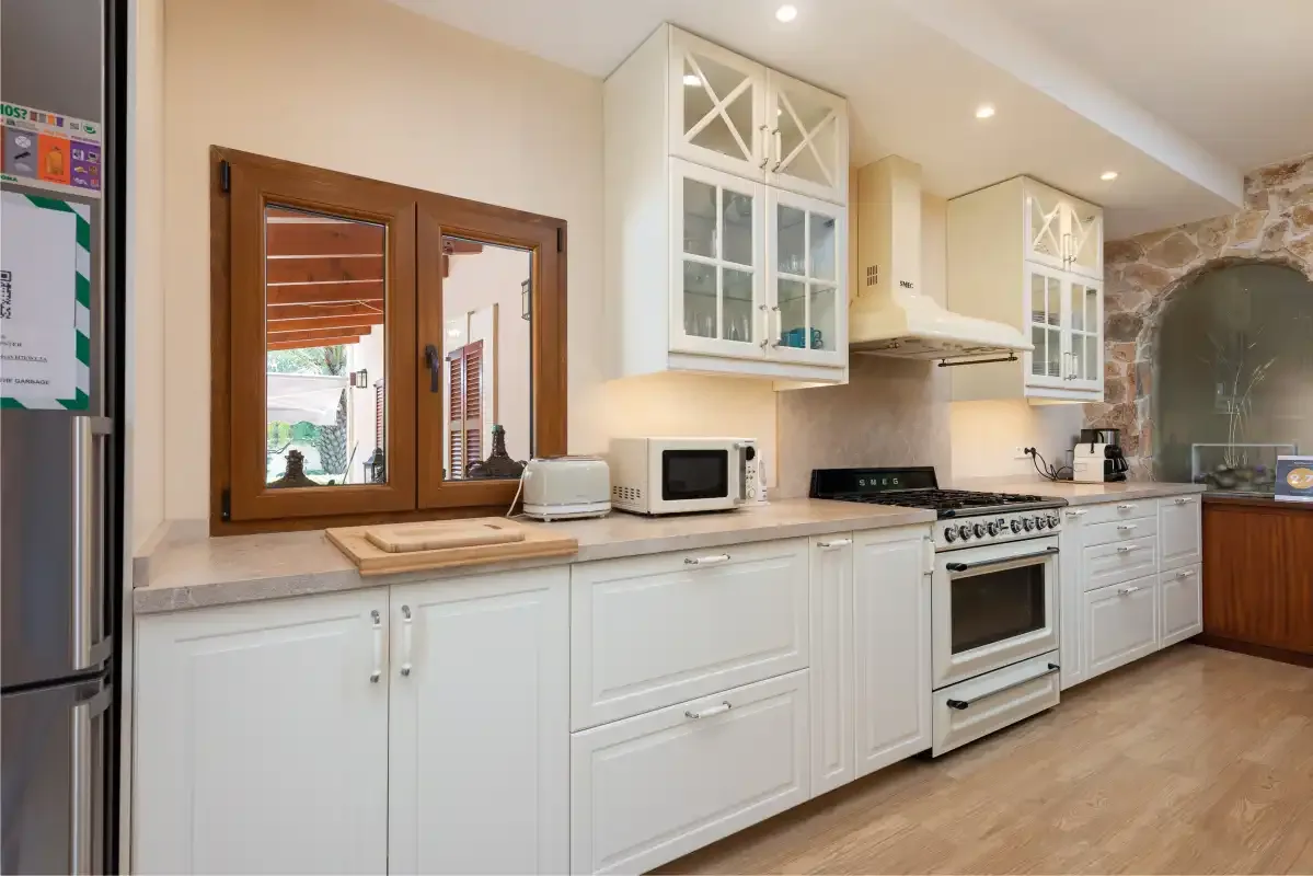 Una cocina luminosa con gabinetes blancos, una estufa y una ventana con marco de madera.