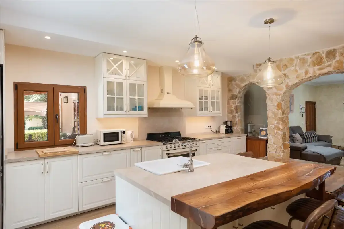Una cocina luminosa con gabinetes blancos, una isla central y una mesa de comedor de madera.
