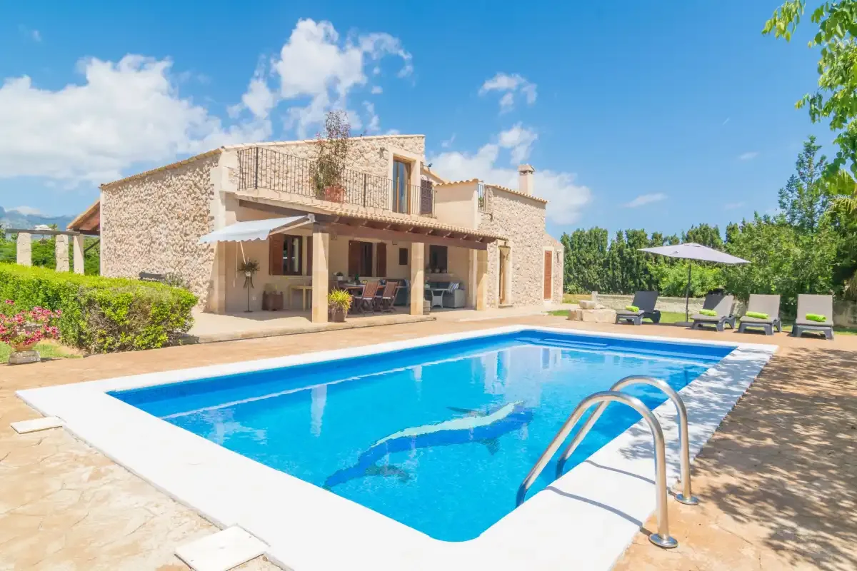 Una casa de piedra da a una piscina con asientos de descanso cerca.