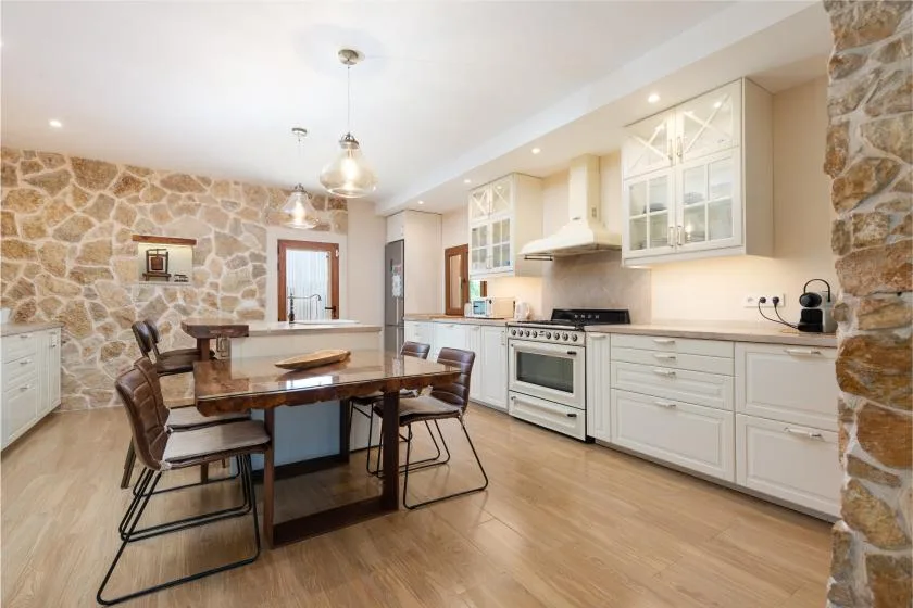 Una cocina y comedor luminosos con gabinetes blancos y una mesa de madera.