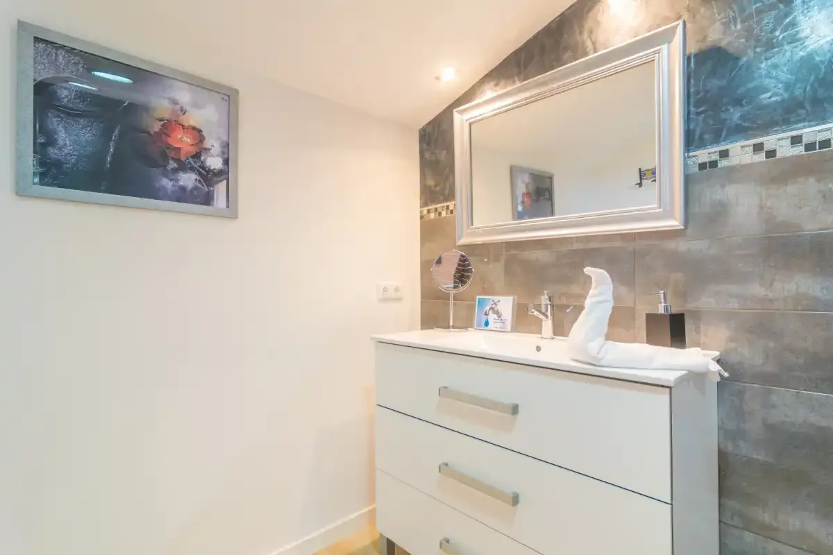 Un tocador de baño con lavabo, espejo grande y una obra enmarcada en la pared.