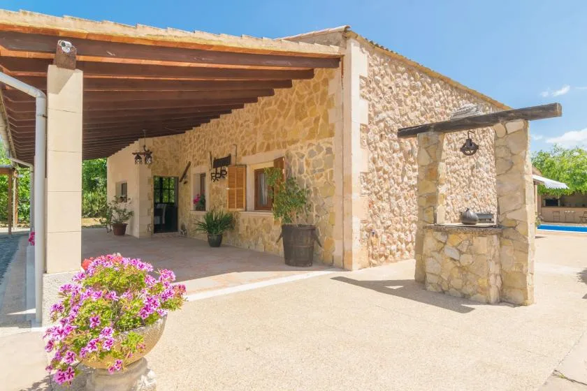 Una casa de piedra con patio cubierto, plantas en macetas y una parrilla exterior.