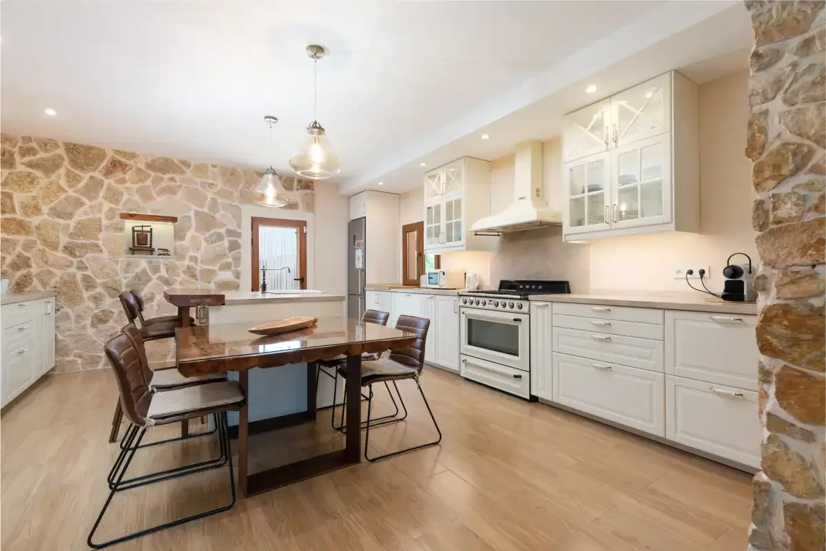 Cocina y comedor con una mesa junto a gabinetes blancos y electrodomésticos.