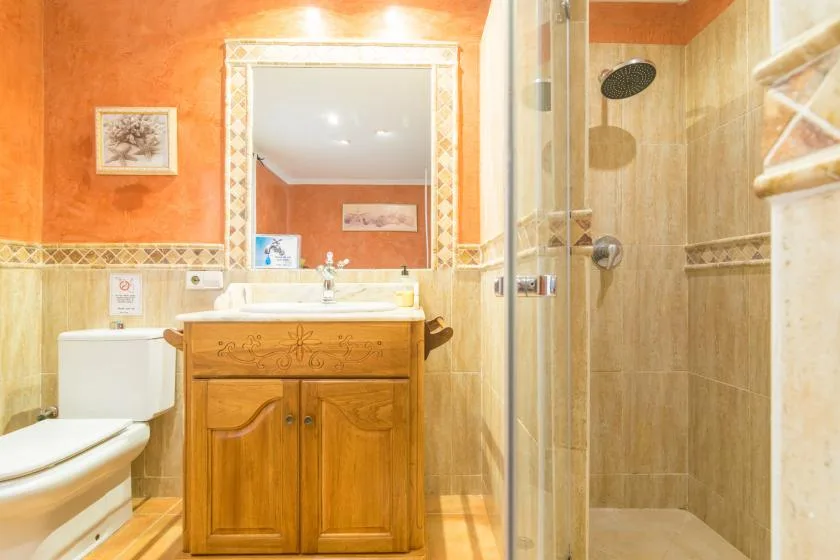Un baño con mueble de madera, lavabo, inodoro y ducha de vidrio.