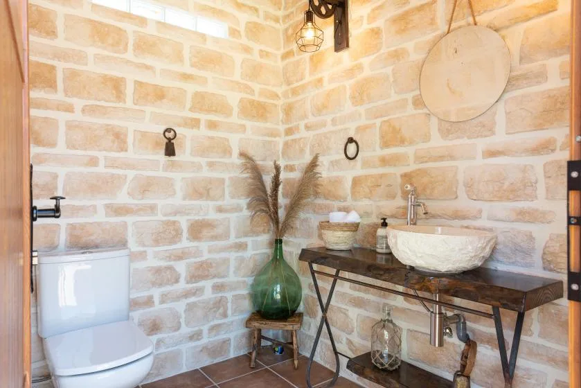Un baño con paredes de piedra, lavabo sobre encimera e inodoro.