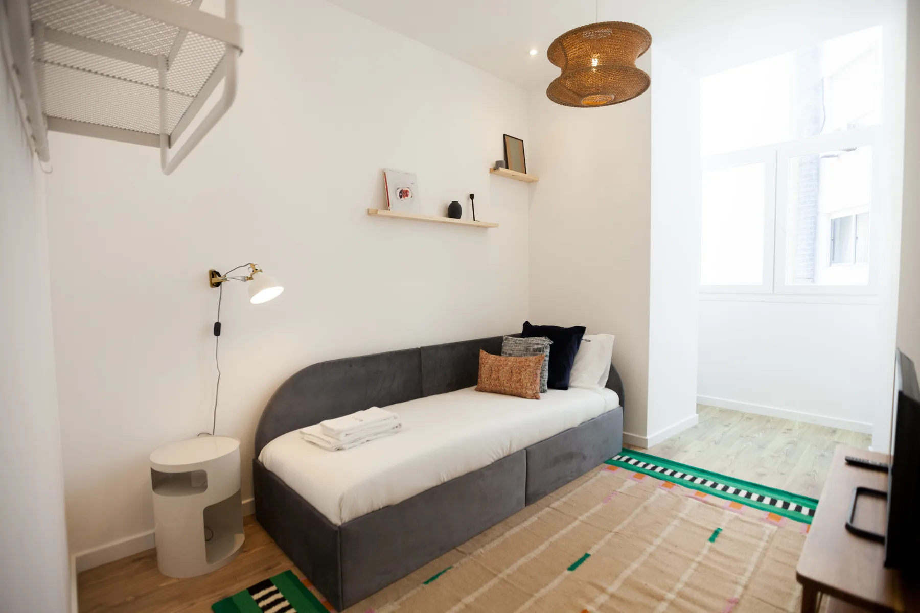 Un dormitorio luminoso con una cama de día, una alfombra tejida y una ventana grande.
