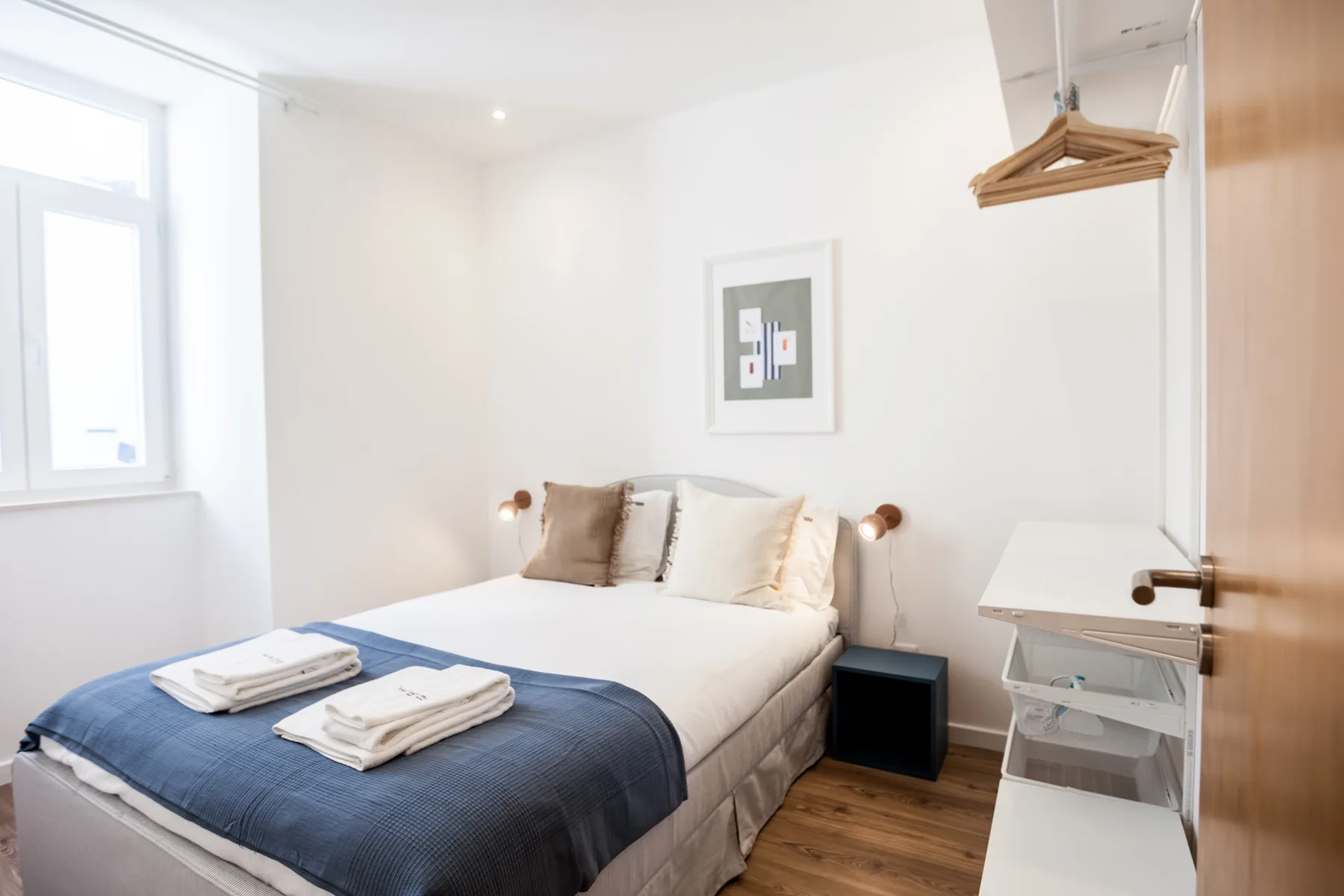 Un dormitorio luminoso con una cama, toallas dobladas y una ventana.