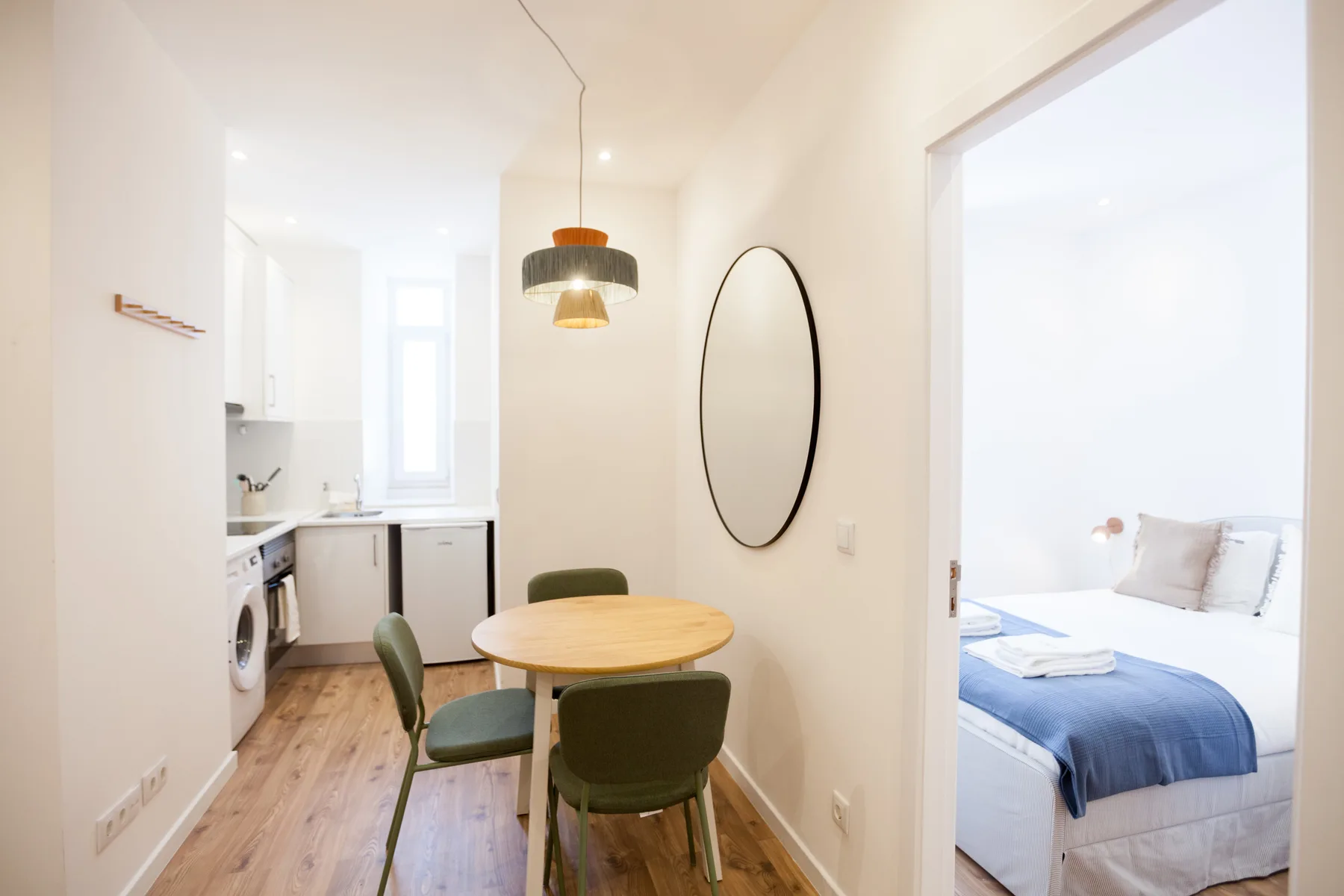 Un comedor con mesa redonda y asientos verdes da a un dormitorio.