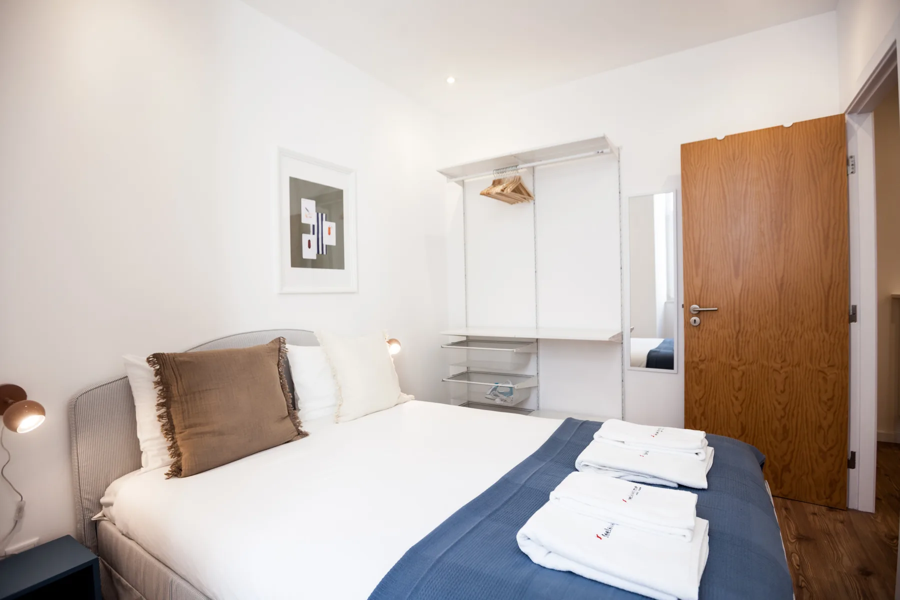 Un dormitorio luminoso con una cama, toallas dobladas y un perchero abierto.