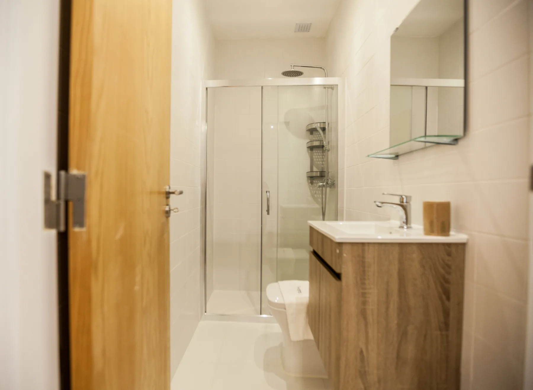Un baño con una ducha de vidrio y un mueble de lavabo en tono madera.