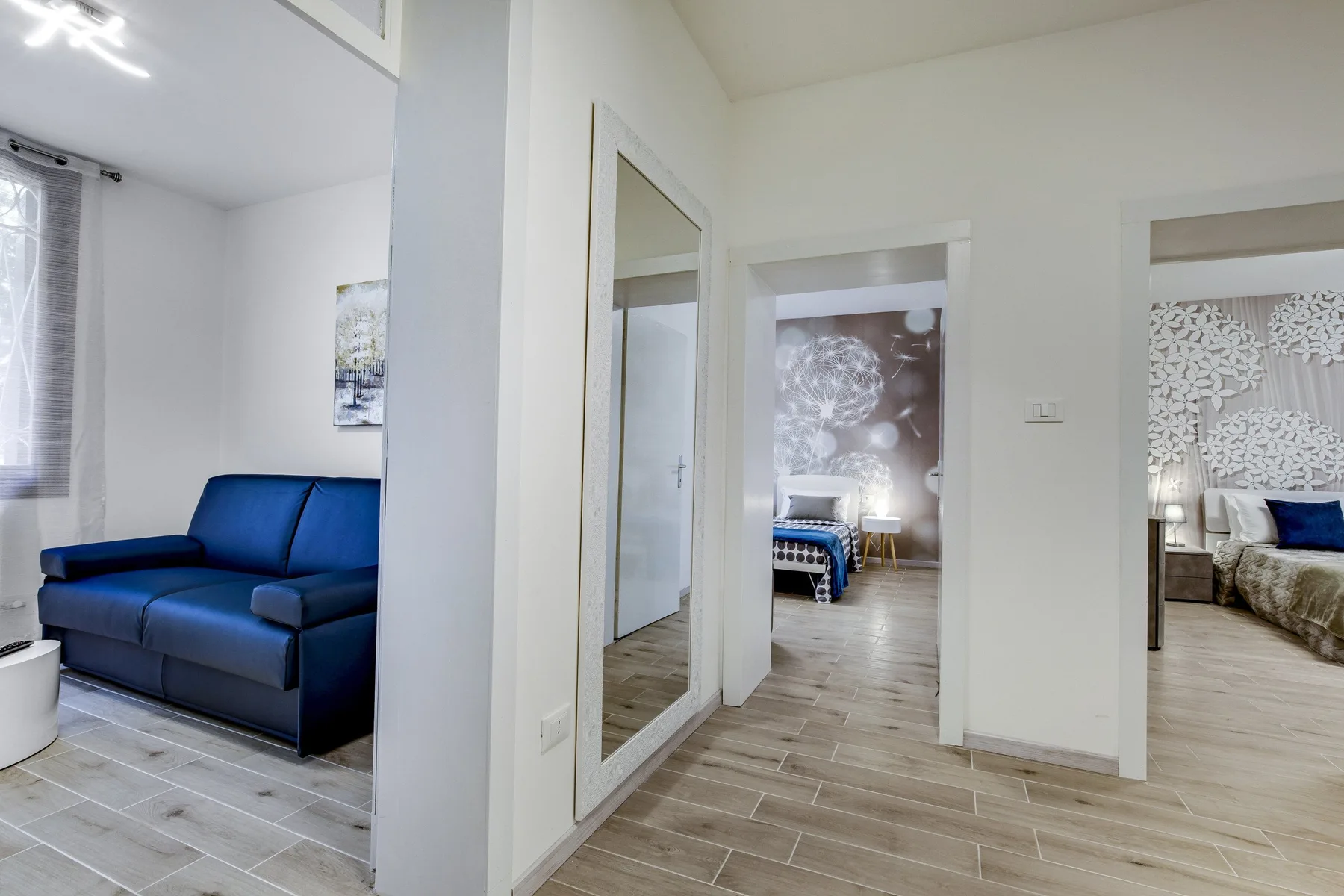 Un pasillo luminoso da acceso a habitaciones con camas y un sofá azul.