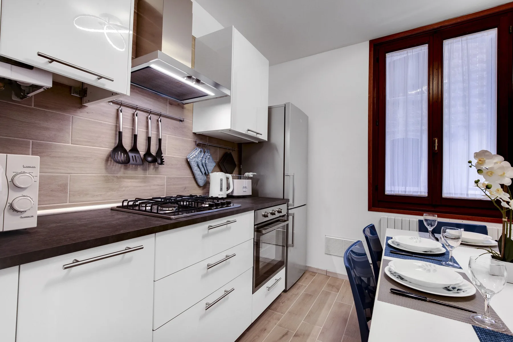 Una cocina moderna con gabinetes blancos y una mesa puesta junto a la ventana.