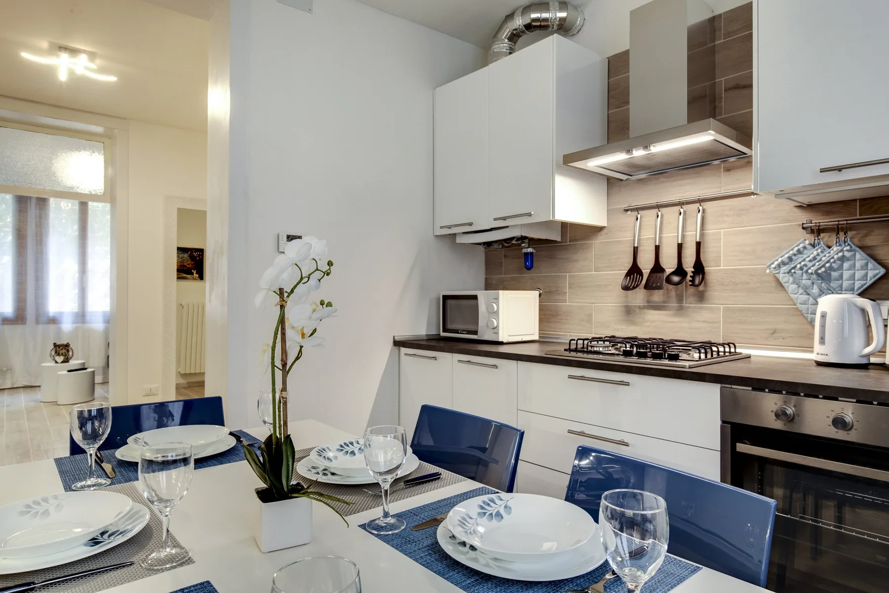 Una mesa de comedor está puesta junto a una cocina moderna con gabinetes blancos y una estufa.