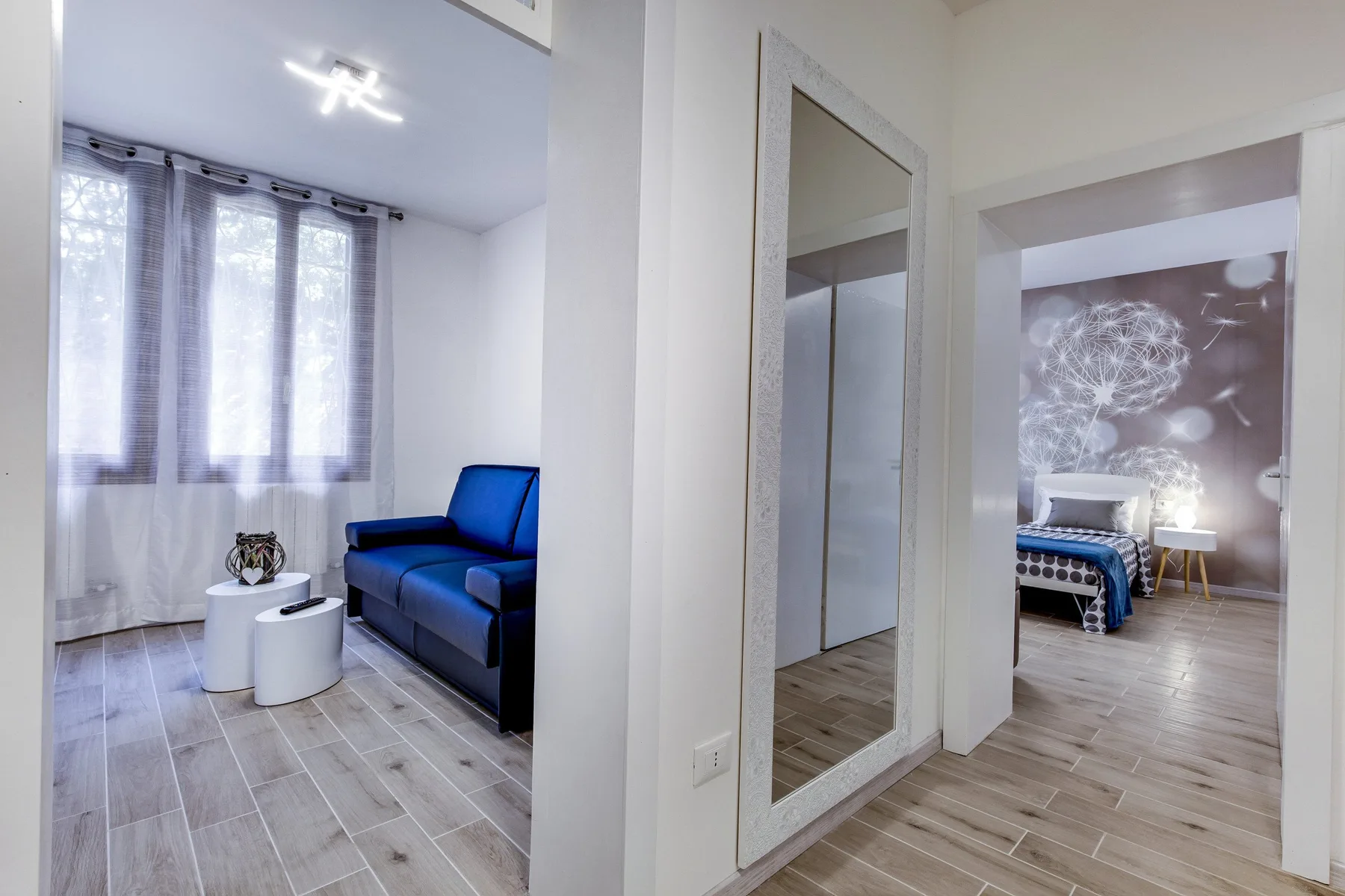 Una sala luminosa con un sofá azul y una puerta que da a un dormitorio.