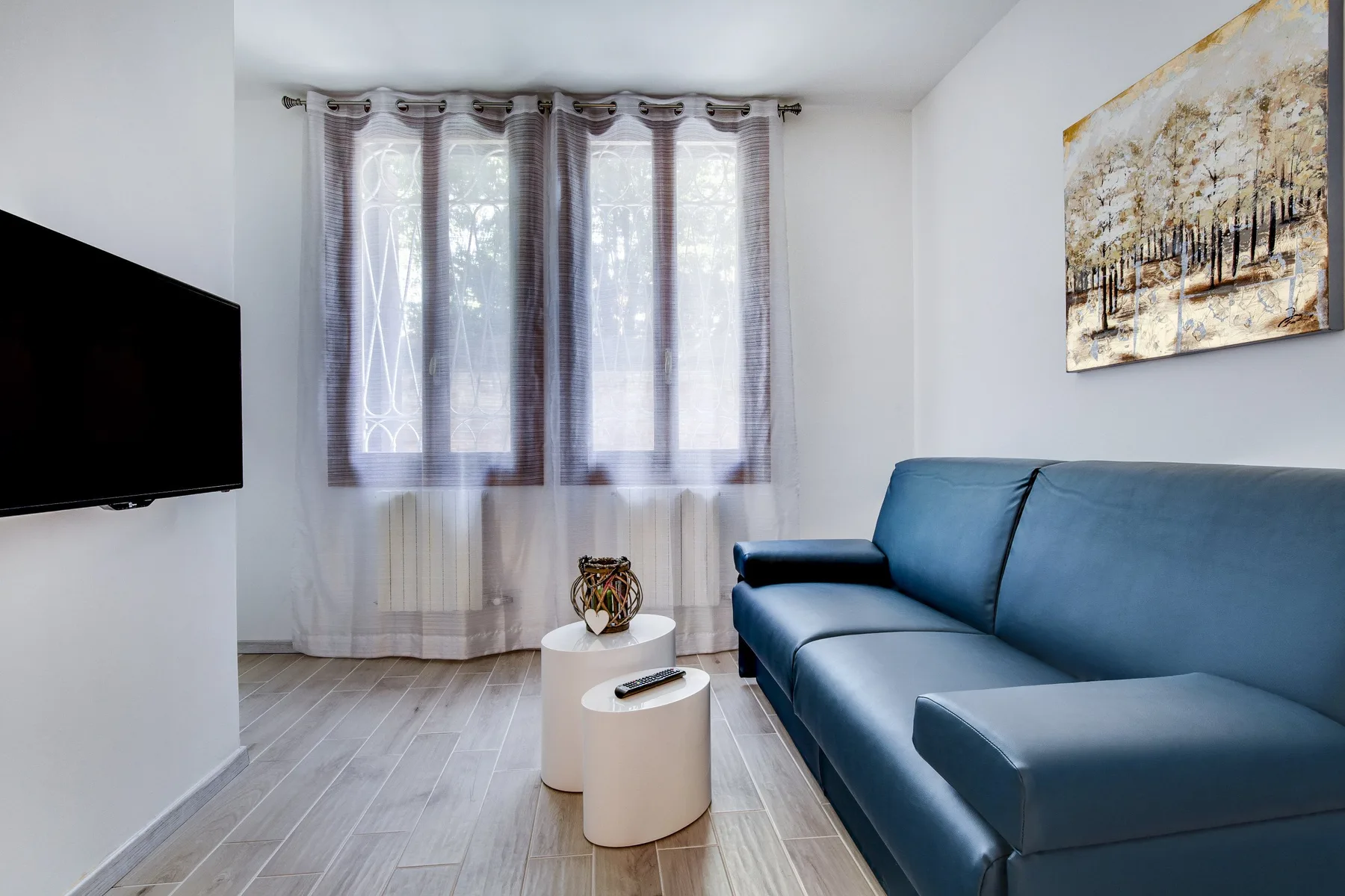 Una sala luminosa con asientos azules, un televisor y grandes ventanas con cortinas.