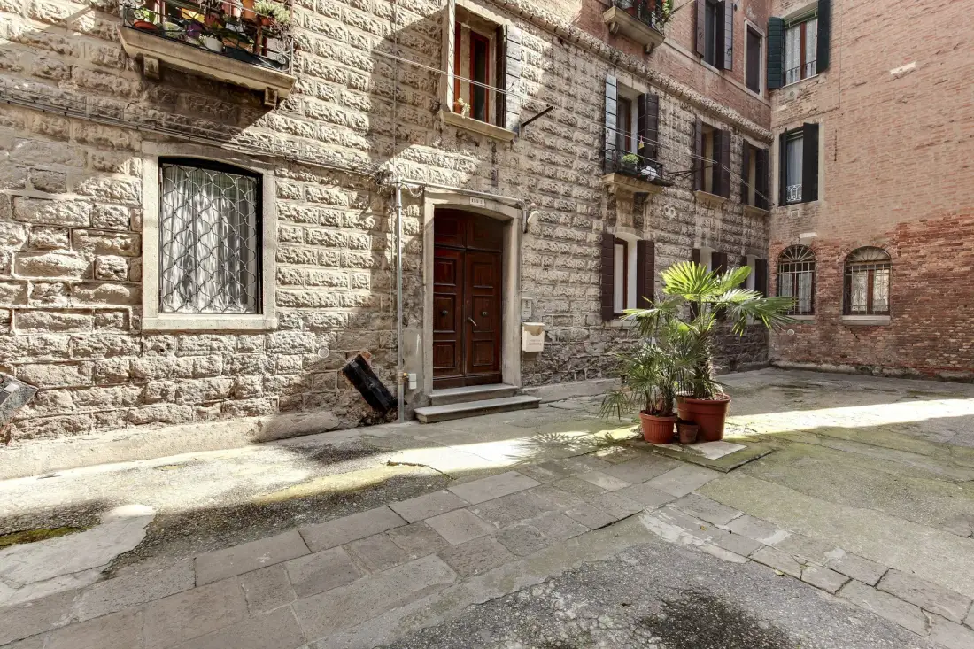 La entrada de un edificio de piedra da a un patio pavimentado con plantas en macetas.