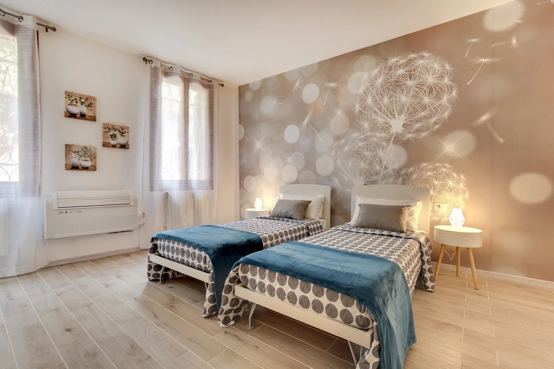 Dormitorio luminoso con dos camas, una pared decorativa estampada y ventanas altas.