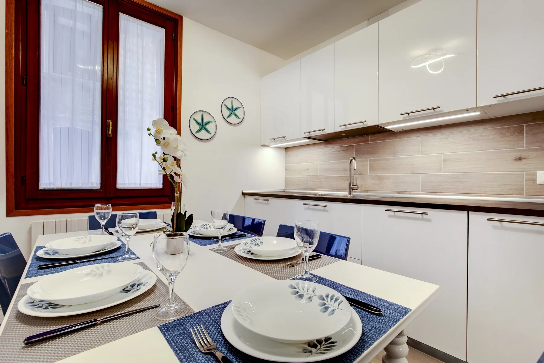 Una mesa está preparada en una cocina luminosa con armarios blancos.