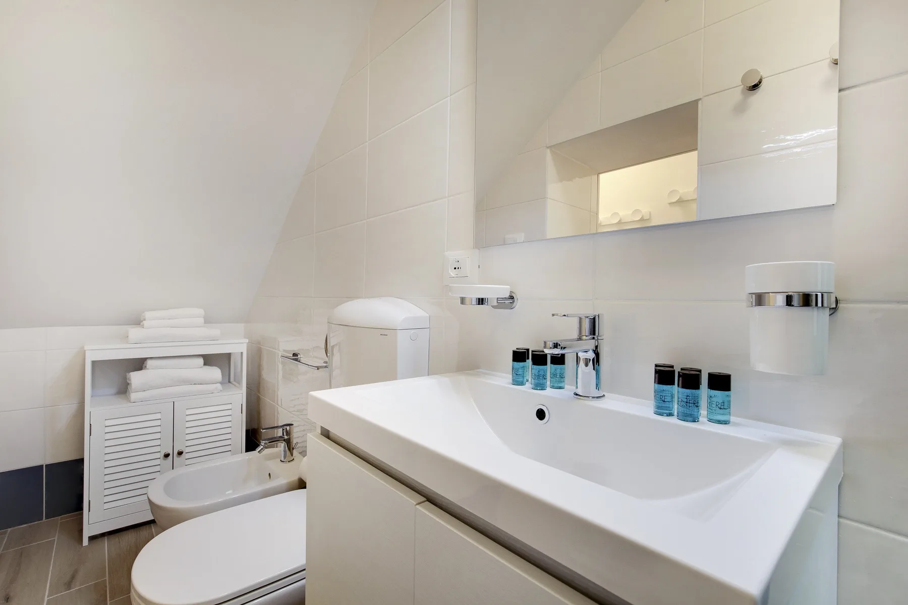 Un baño luminoso con un lavabo grande, un espejo y paredes de azulejos blancos.