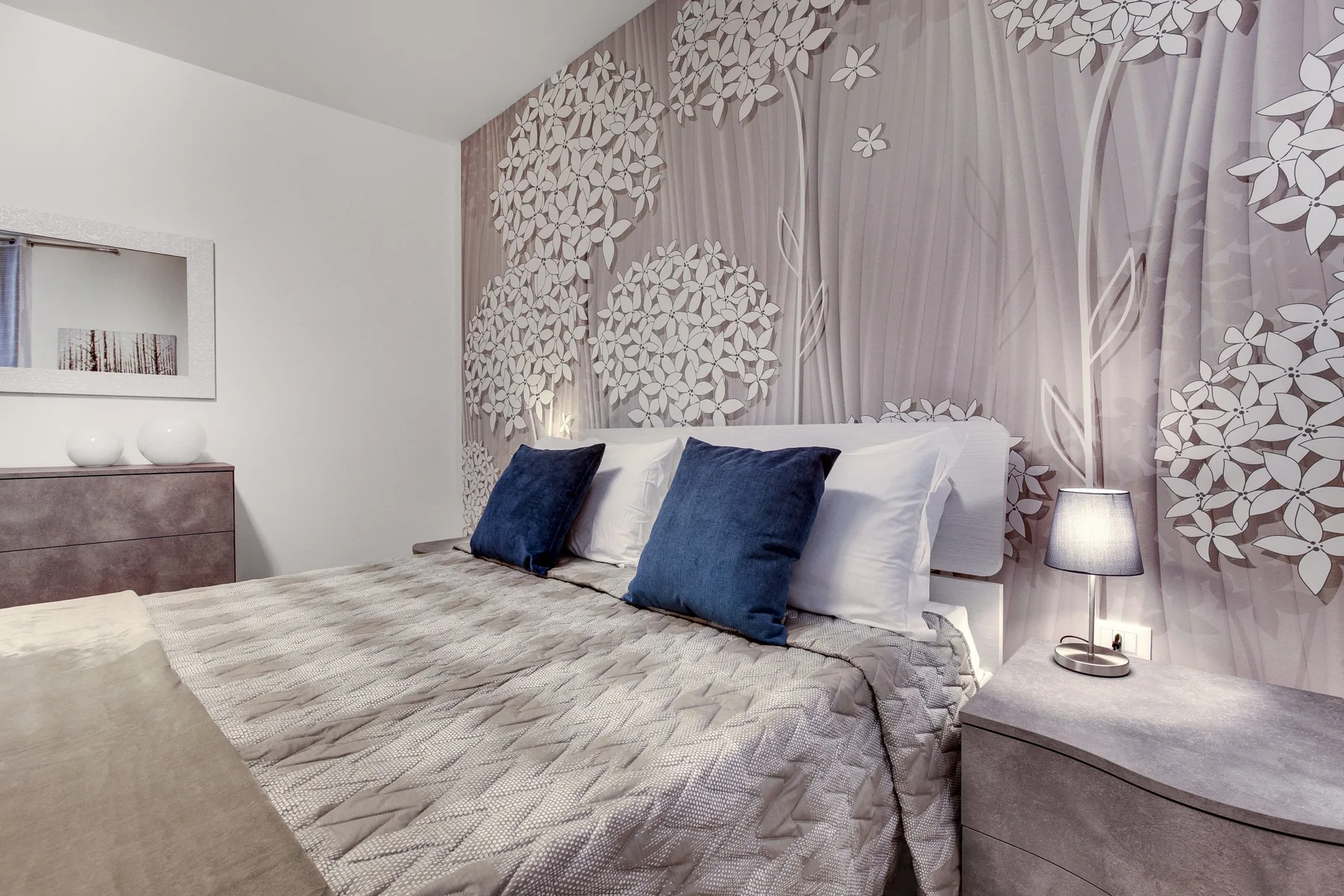 Un dormitorio con una cama bien tendida y una pared con motivos florales detrás.