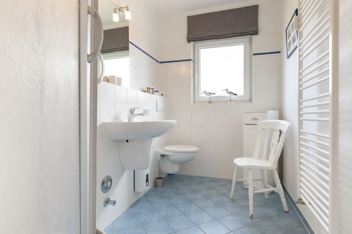A bright tiled bathroom with a sink, toilet, and window.