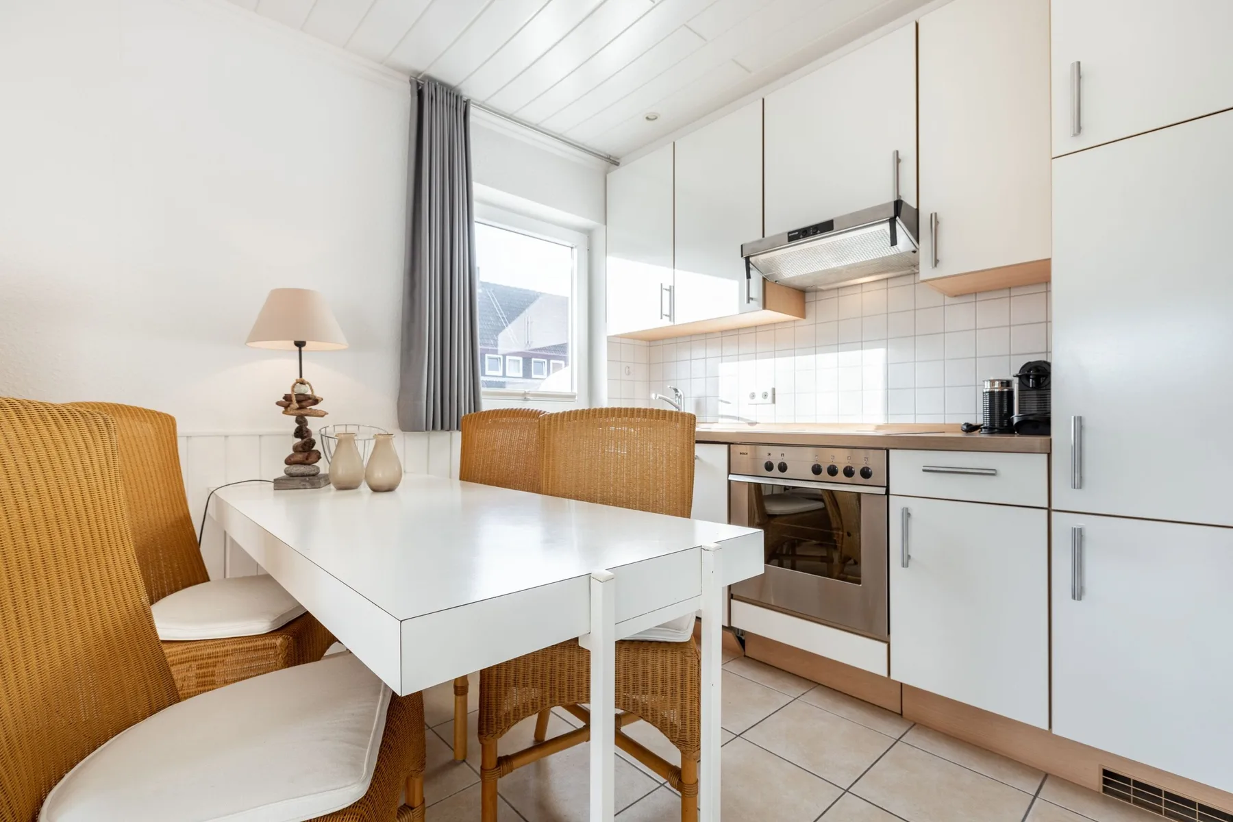 A bright kitchen and dining area with a white table and woven seating.