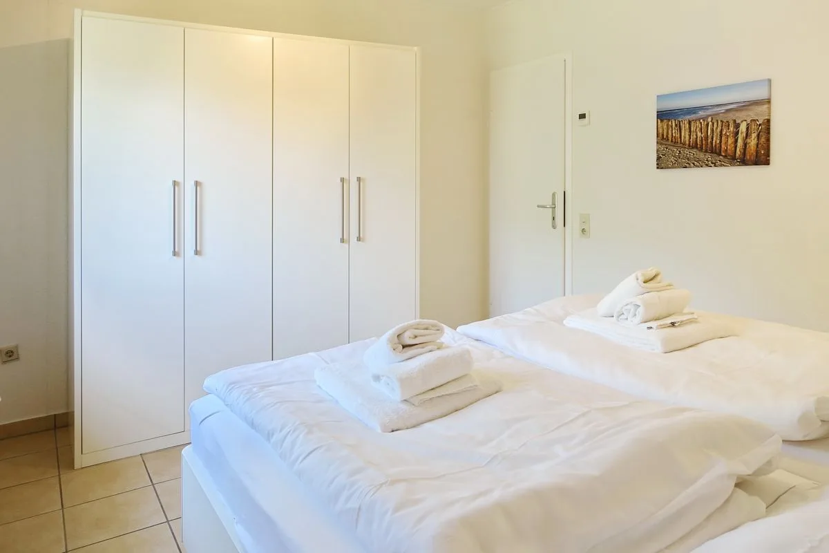 A bright bedroom with white bedding and built-in wardrobes.