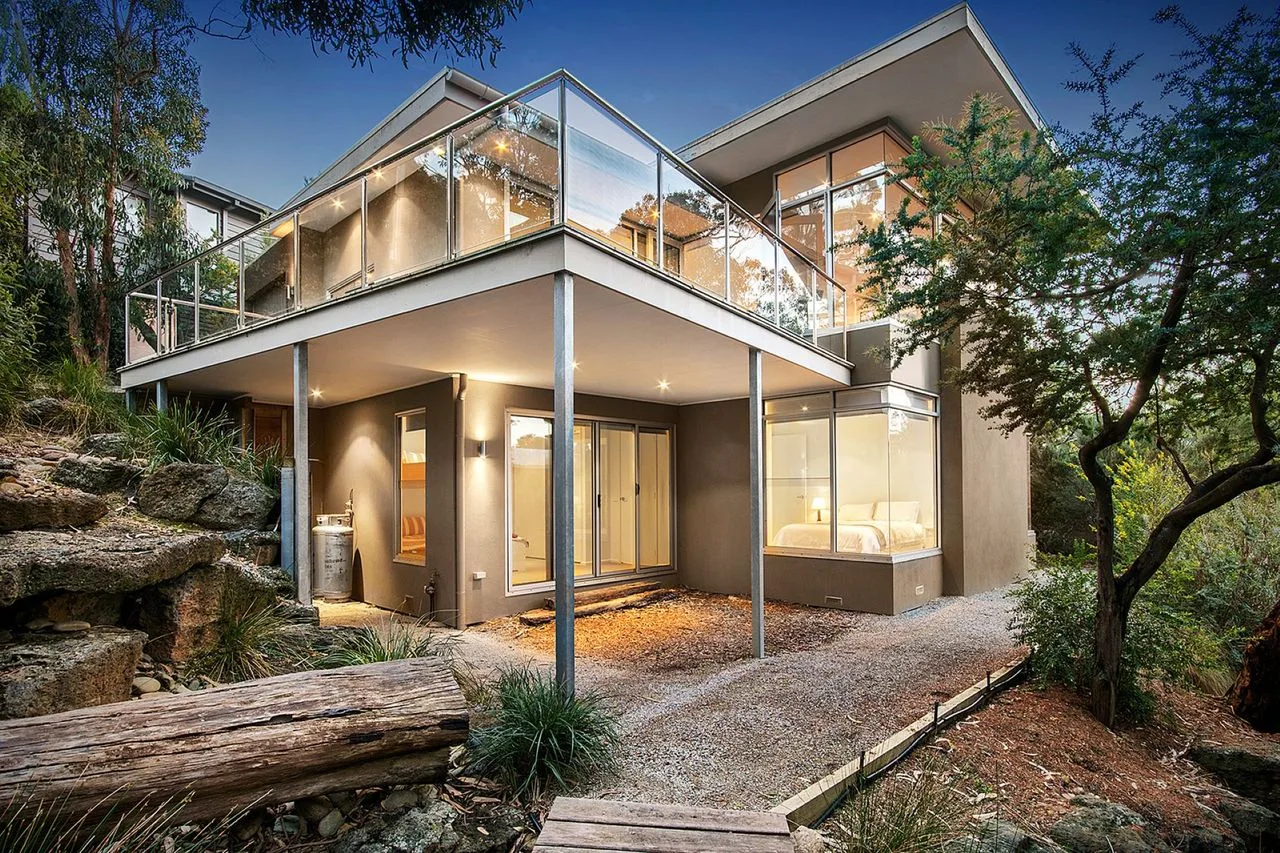 Modern house with glass balconies set among trees and rocks.