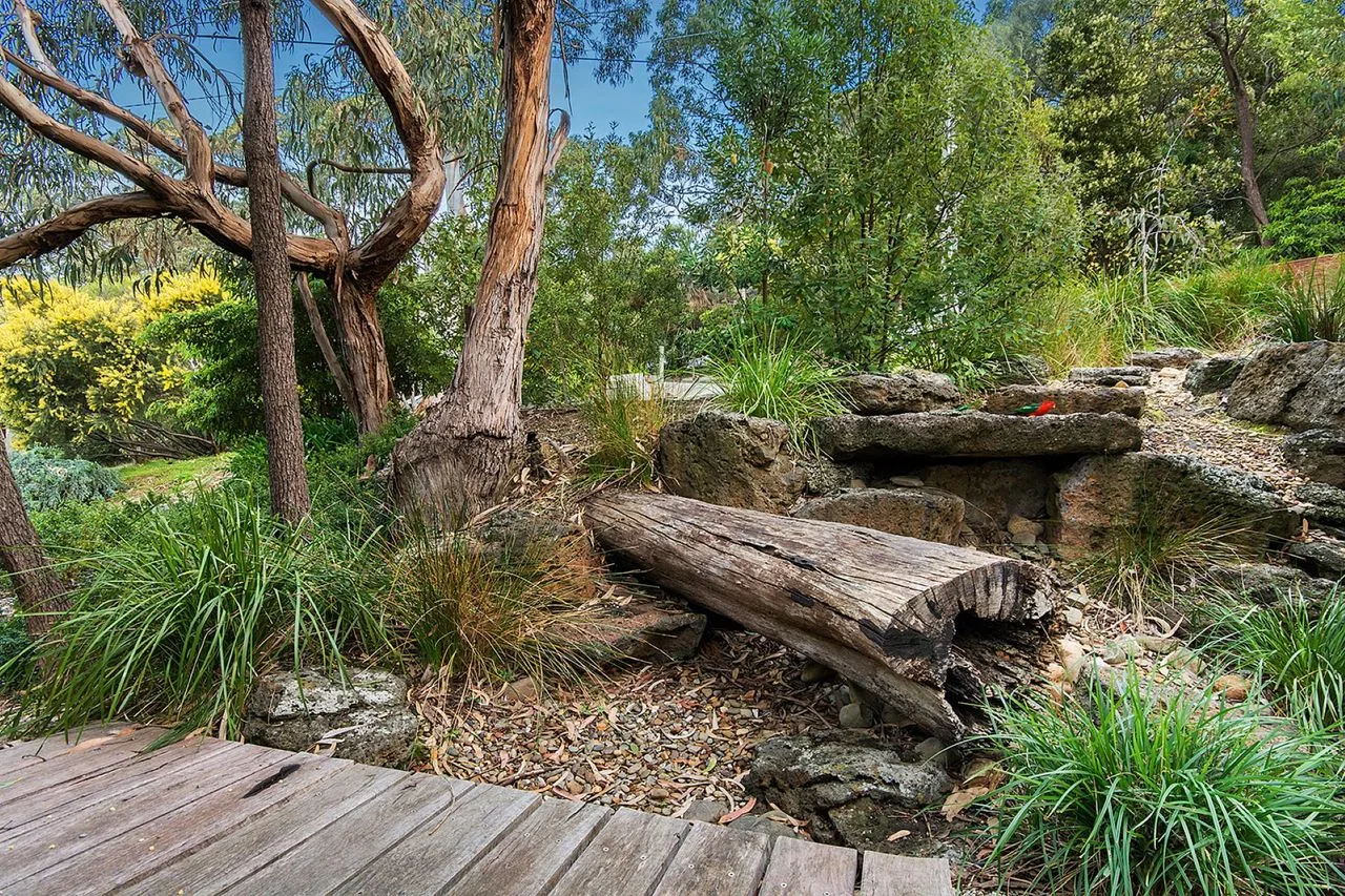 A garden seating area with a log bench among trees and rocks.