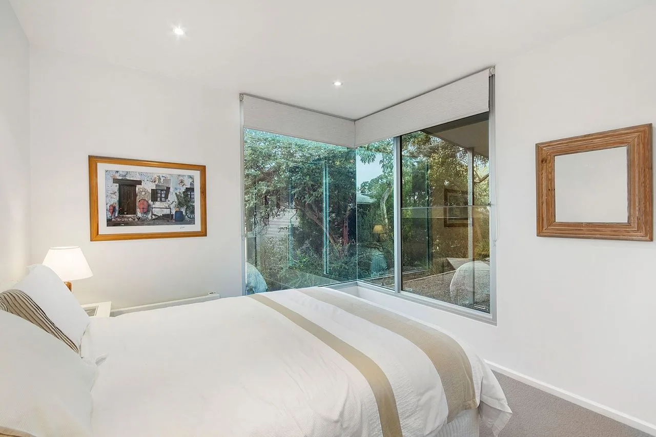 A bright bedroom with a bed beside large windows overlooking greenery.