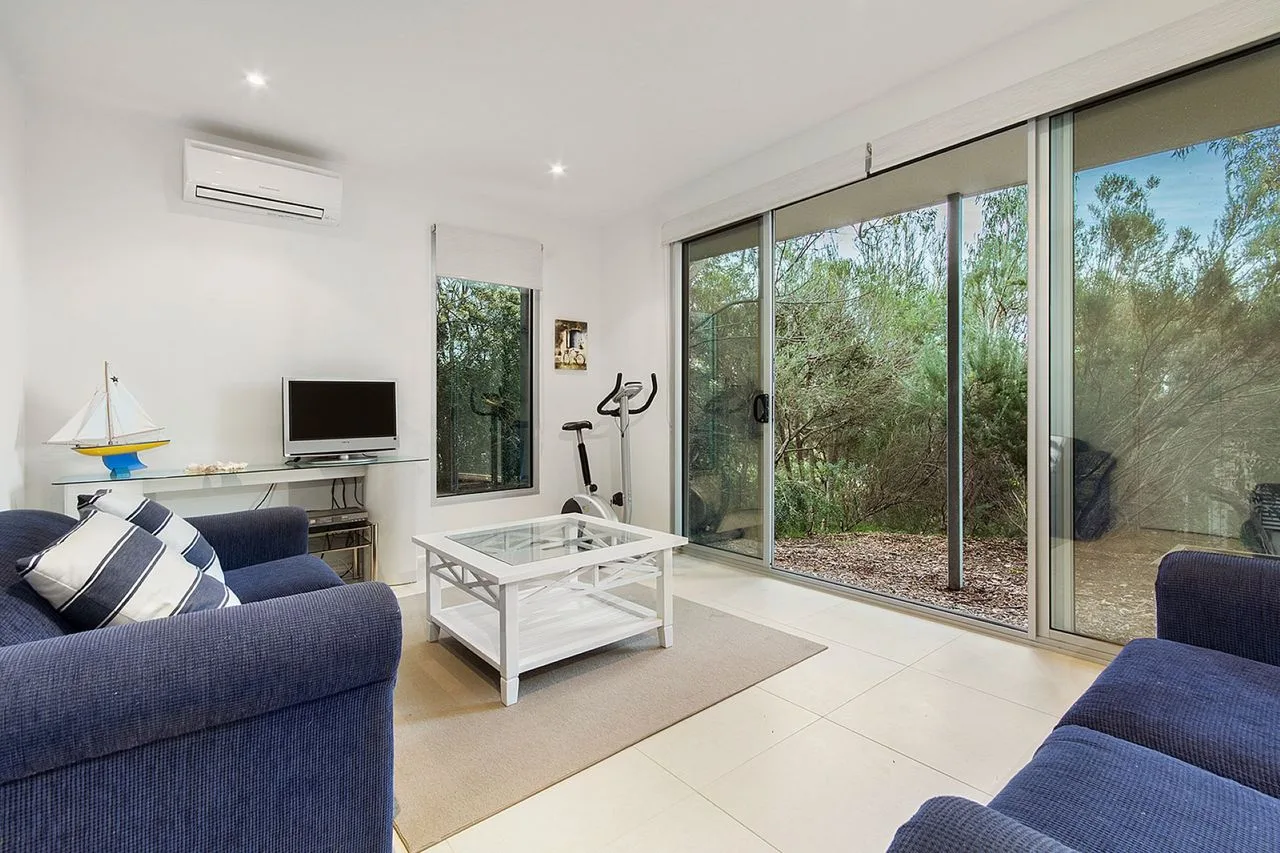 A bright living room with blue seating and large glass doors opening to greenery.