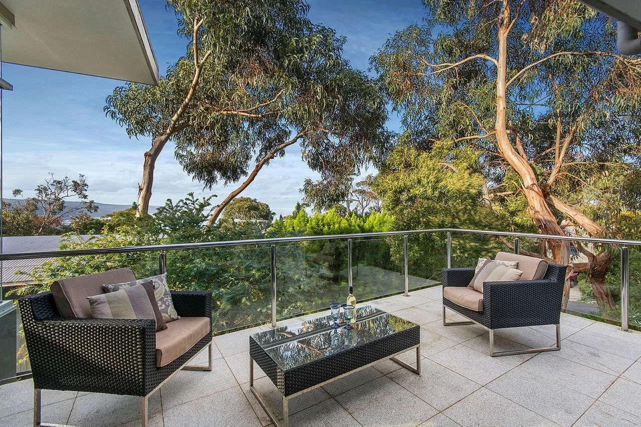 An outdoor seating area with a glass railing and leafy trees beyond.