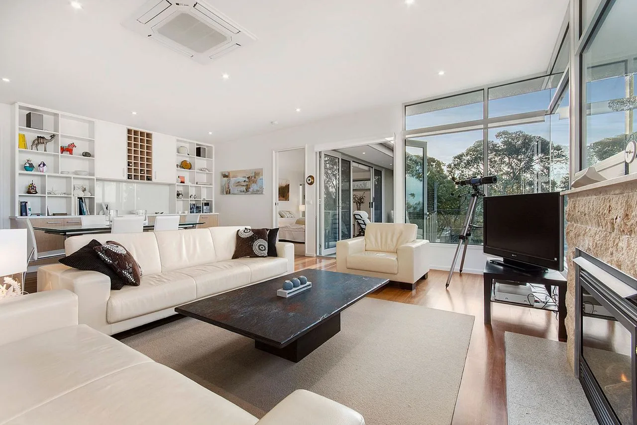 A bright living room with seating, a coffee table, and large windows.