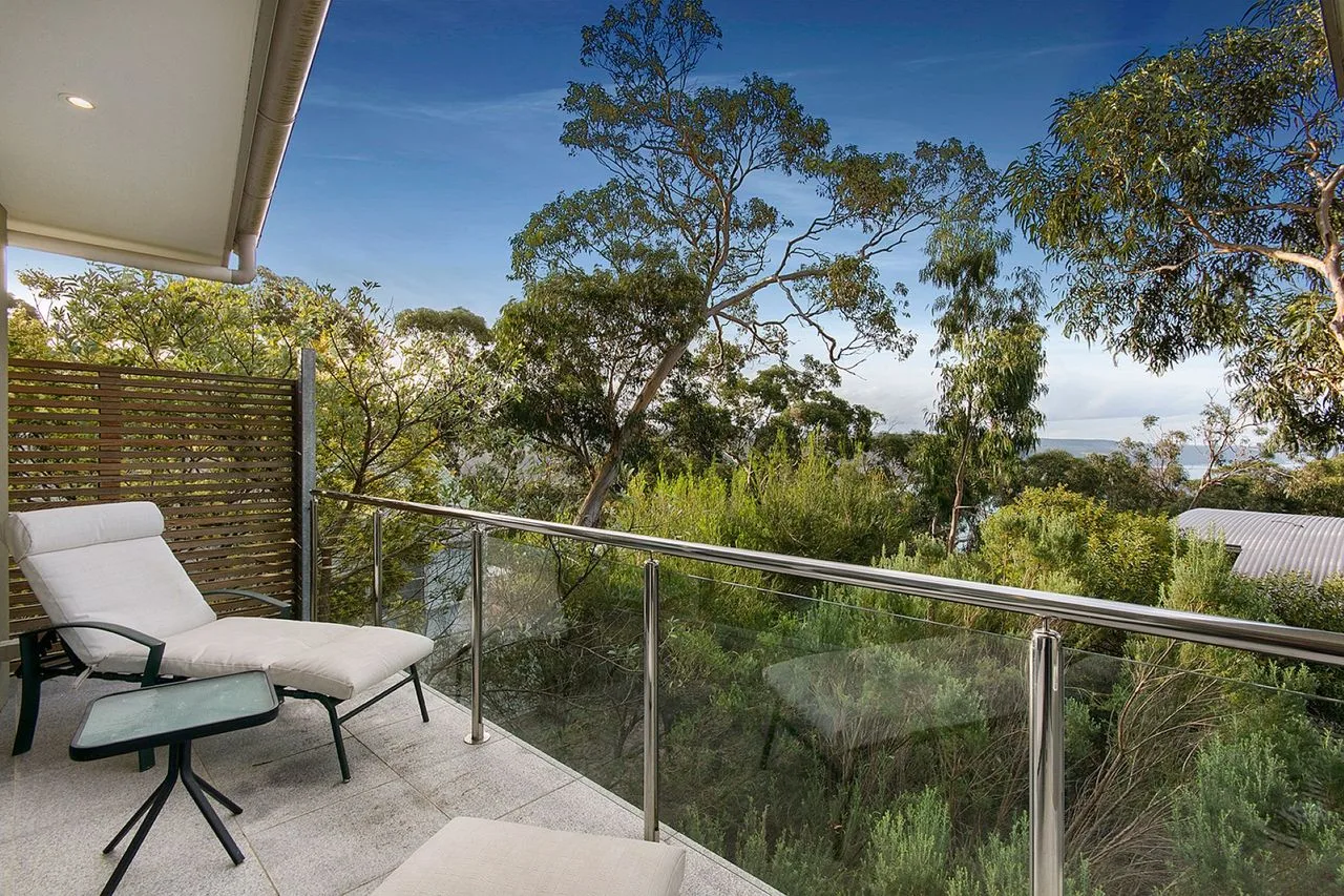 A balcony with outdoor seating overlooks trees and greenery.
