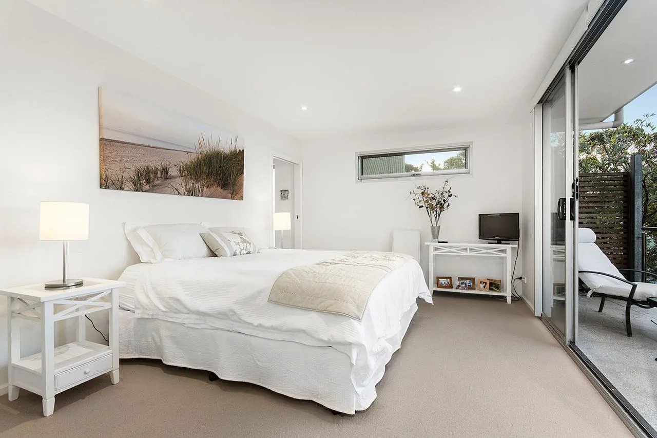 A bright bedroom with white bedding and sliding glass doors opening onto a patio.