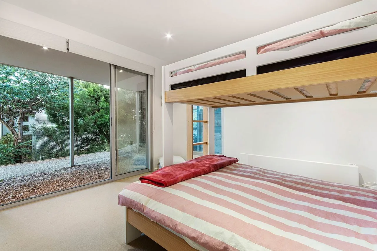 A bedroom with a striped bed beneath a wooden loft bed.