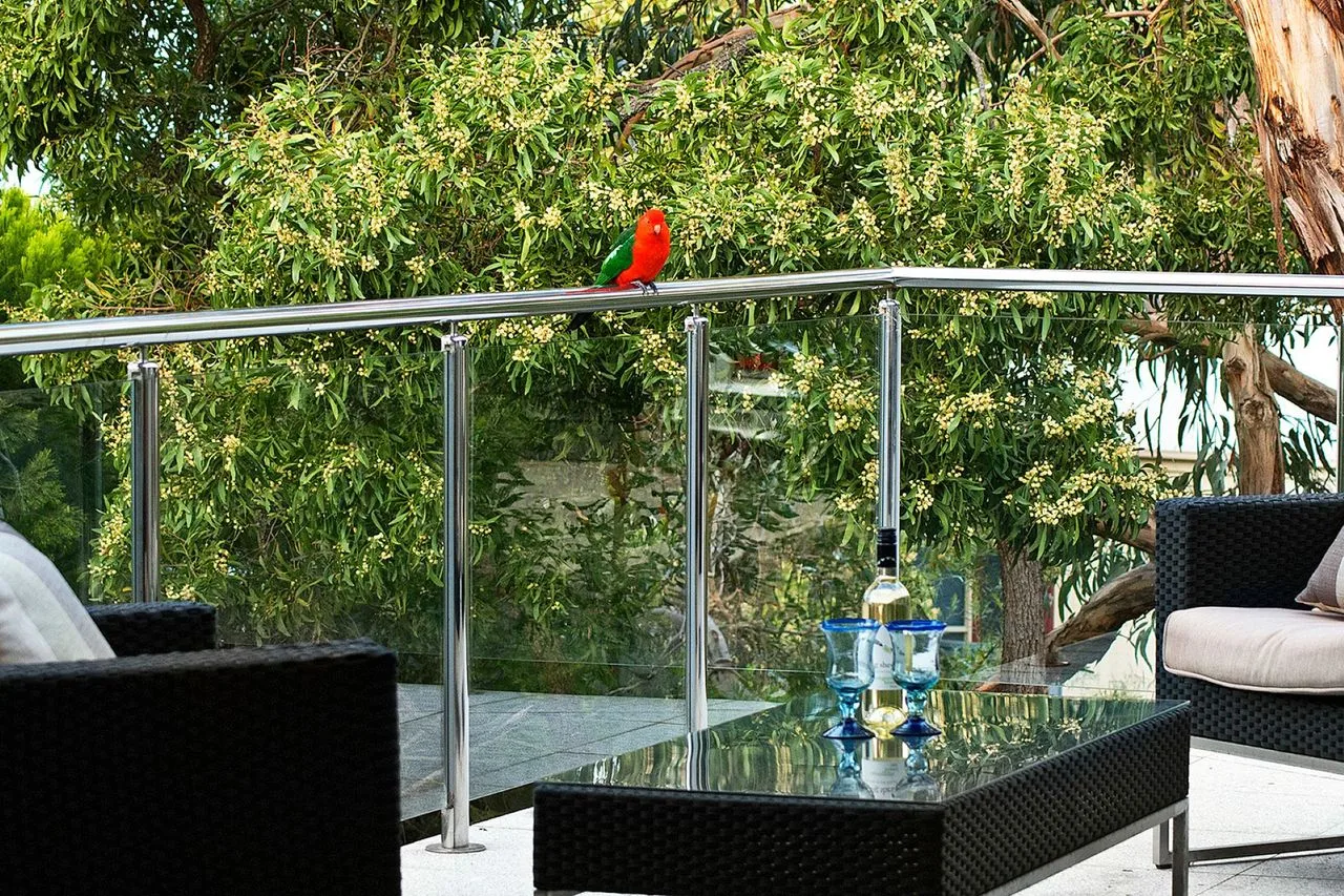 A patio seating area with a glass table overlooks leafy trees.