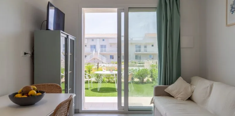 A bright living room with a white sofa, television, and sliding glass doors.
