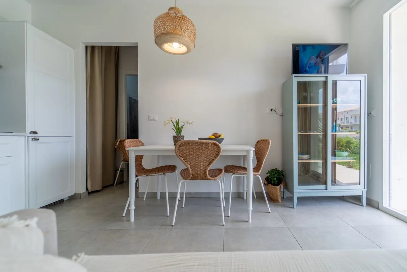 A bright dining area with a table, woven seating, and a glass-front cabinet.