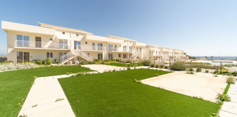 A row of low-rise residential buildings overlooks landscaped lawns and paved walkways.