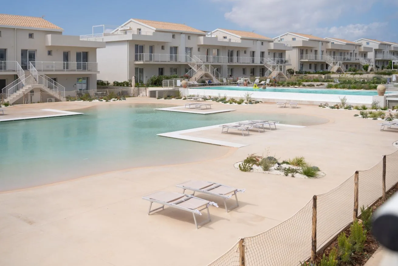 A large outdoor swimming pool with lounge seating is surrounded by apartment buildings.