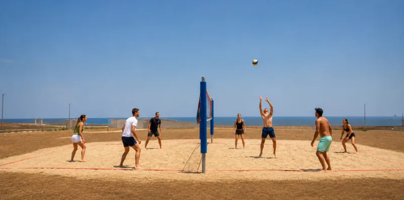 People play volleyball on a sandy beach court beside the sea.