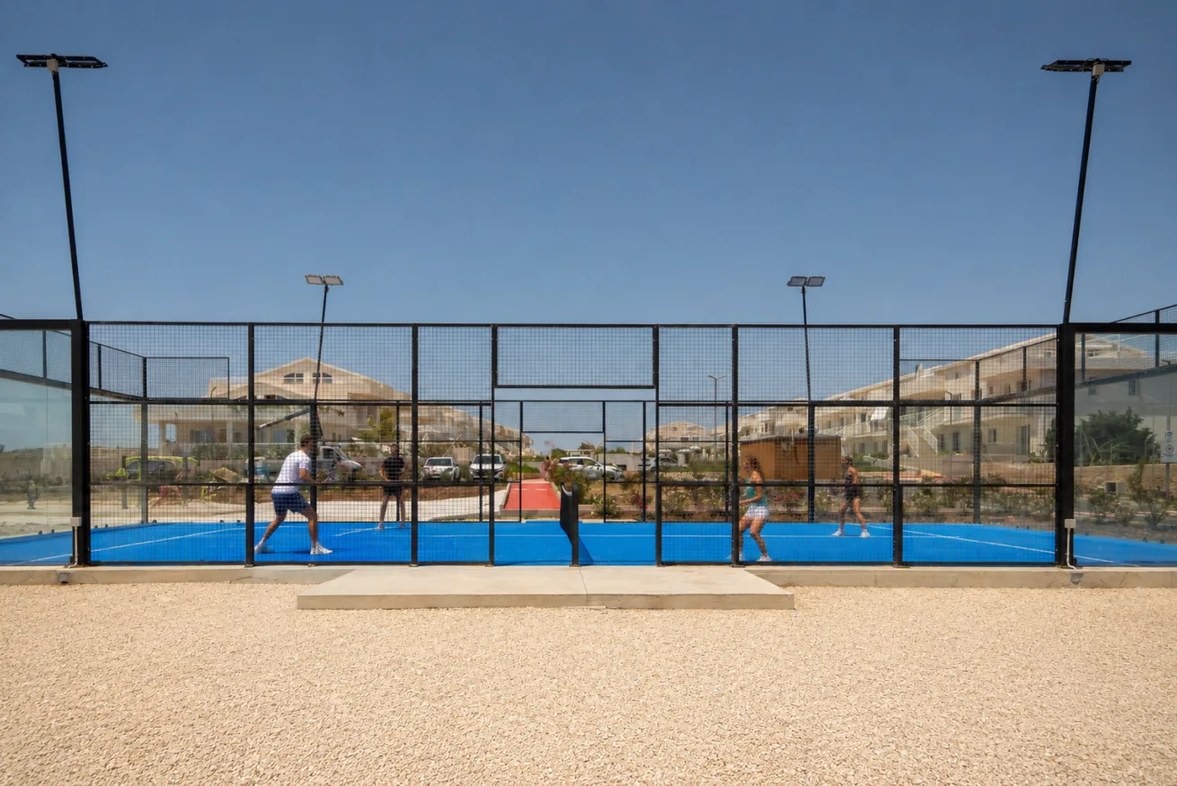 A fenced outdoor sports court with people playing on a blue surface.