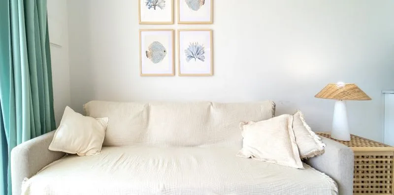 A bright living room with a cream sofa, teal curtains, and framed wall art.