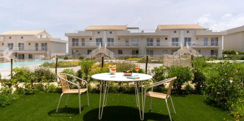 A garden seating area with a round table overlooks a swimming pool and apartment buildings.